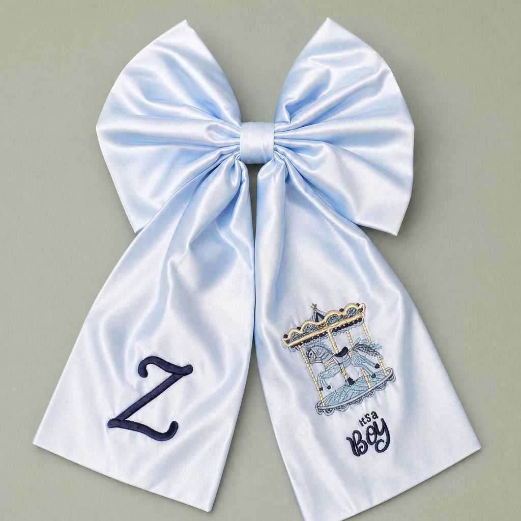 Oversized ice blue silk announcement bow with a navy embroidered initial on one tail and a carousel with It's a Boy lettering on the other