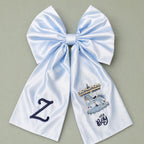 Oversized ice blue silk announcement bow with a navy embroidered initial on one tail and a carousel with It's a Boy lettering on the other