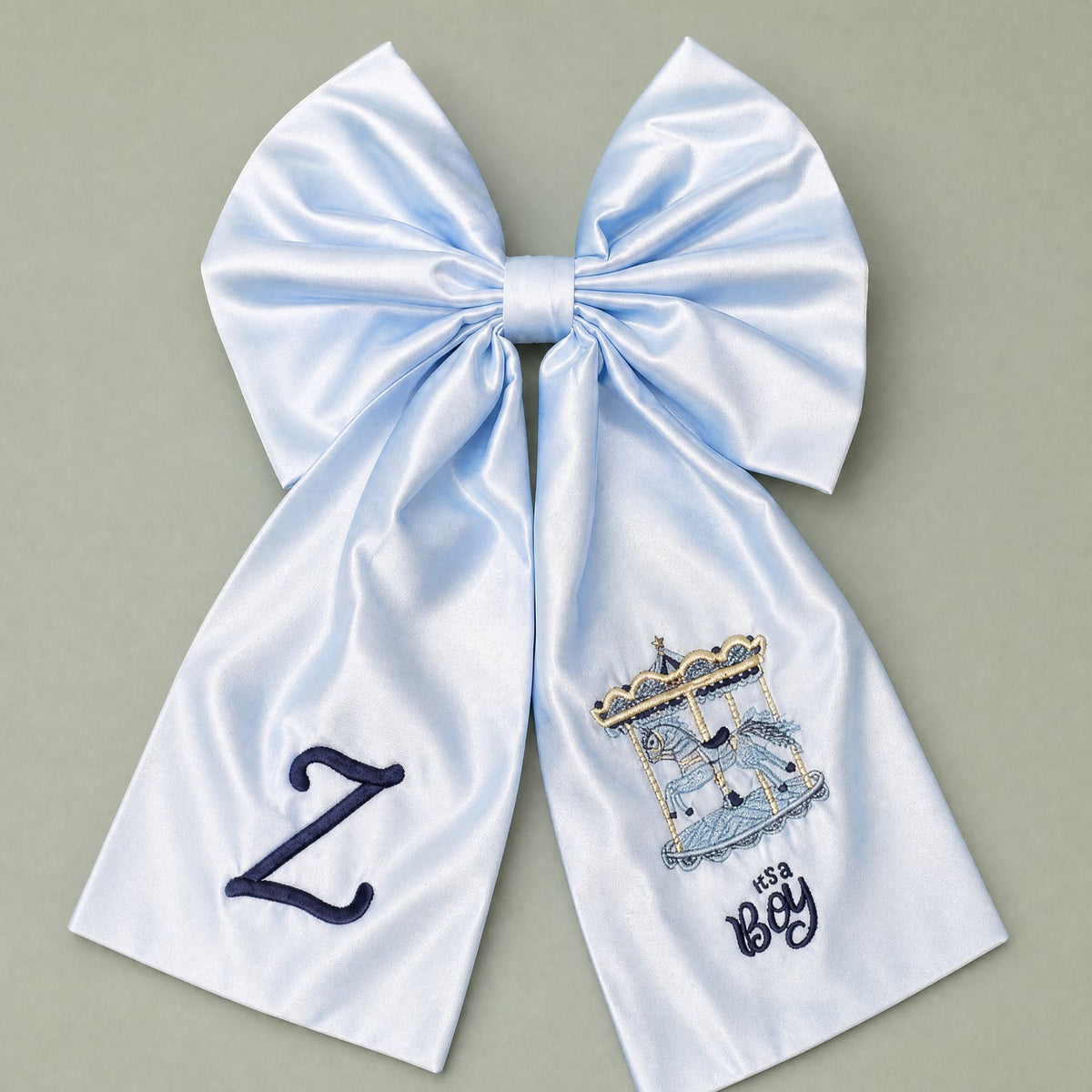 Oversized ice blue silk announcement bow with a navy embroidered initial on one tail and a carousel with It's a Boy lettering on the other