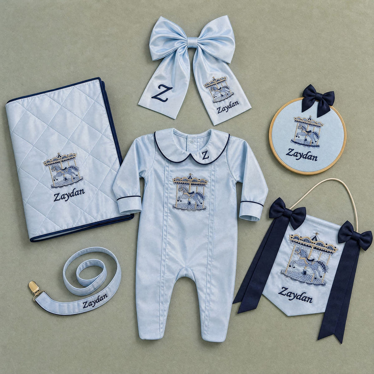 The Grand Arrival ice blue gift bundle laid out flat — all six personalised ice blue silk pieces including romper, wrapping sheet, name frame, name flag, announcement bow and pacifier holder