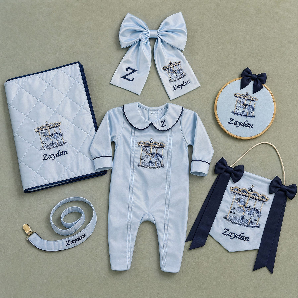 The Grand Arrival ice blue gift bundle laid out flat — all six personalised ice blue silk pieces including romper, wrapping sheet, name frame, name flag, announcement bow and pacifier holder