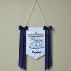Ice blue silk name flag with an embroidered carousel, silk bows and a baby's name in navy script