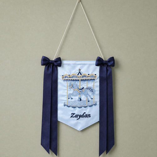 Ice blue silk name flag with an embroidered carousel, silk bows and a baby's name in navy script