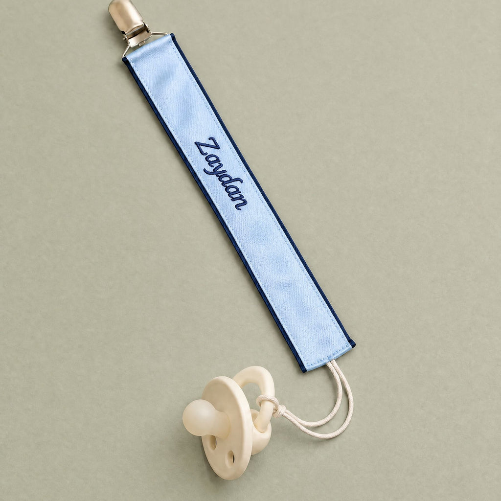 Ice blue silk pacifier holder with navy detailing and a baby's name embroidered in navy script