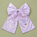 Oversized lilac silk announcement bow with an ivory embroidered initial on one tail and a hot air balloon with It's a Girl lettering on the other