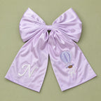Oversized lilac silk announcement bow with an ivory embroidered initial on one tail and a hot air balloon with It's a Girl lettering on the other