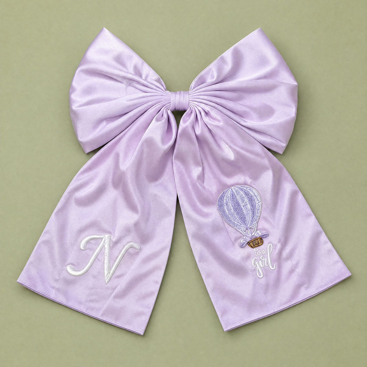 Oversized lilac silk announcement bow with an ivory embroidered initial on one tail and a hot air balloon with It's a Girl lettering on the other
