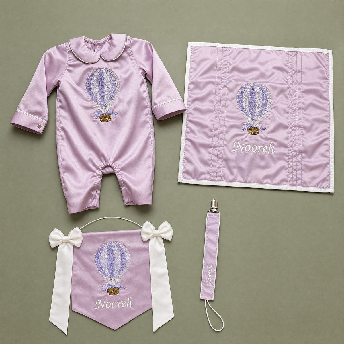 Welcome to the World lilac gift bundle laid out flat — personalised lilac silk romper, wrapping sheet, name flag and pacifier holder