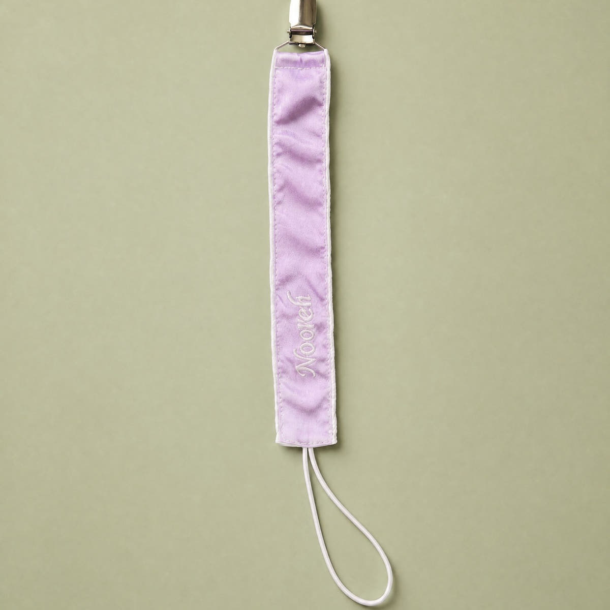 Lilac silk pacifier holder with ivory detailing and a baby's name embroidered in ivory script