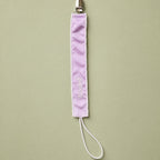 Lilac silk pacifier holder with ivory detailing and a baby's name embroidered in ivory script