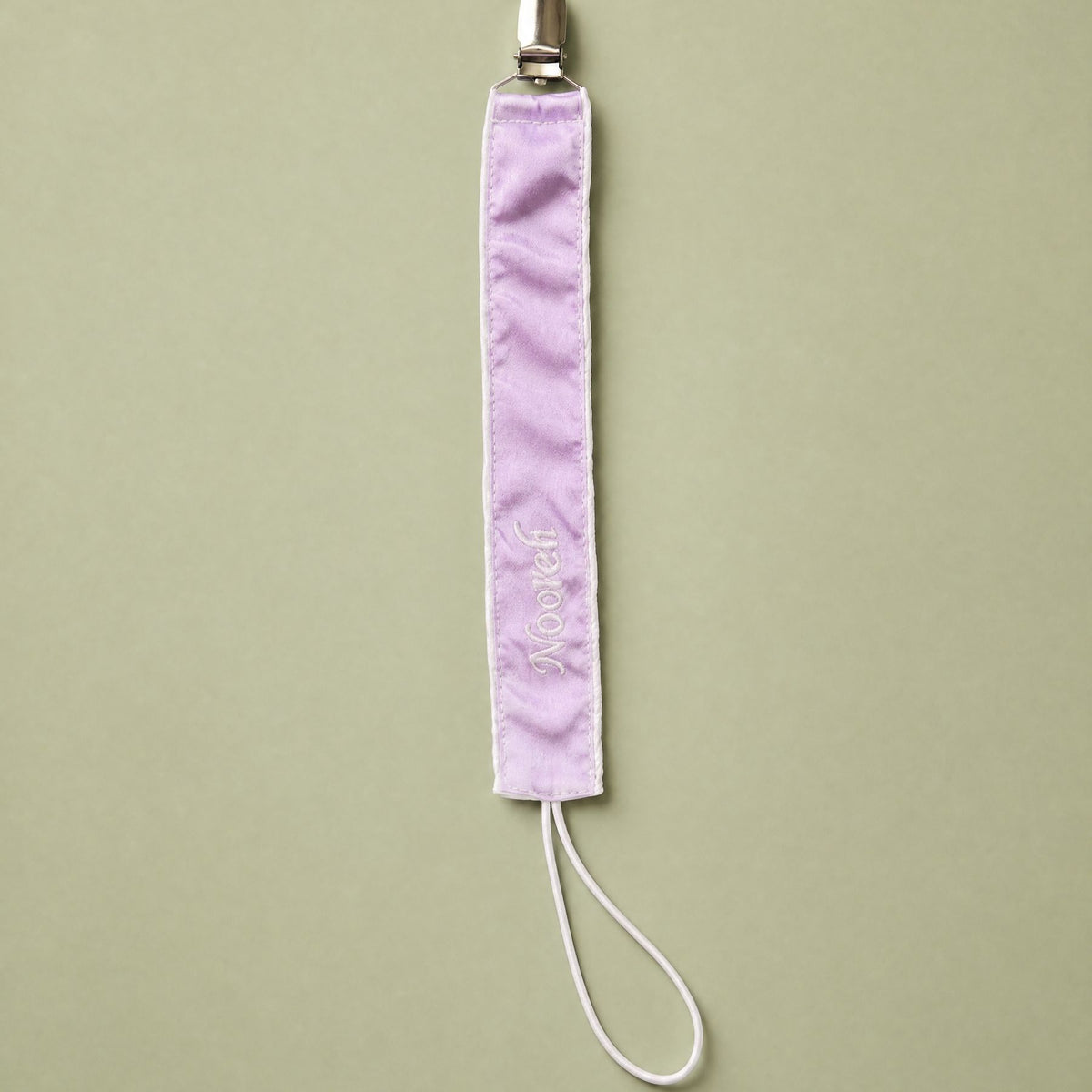 Lilac silk pacifier holder with ivory detailing and a baby's name embroidered in ivory script