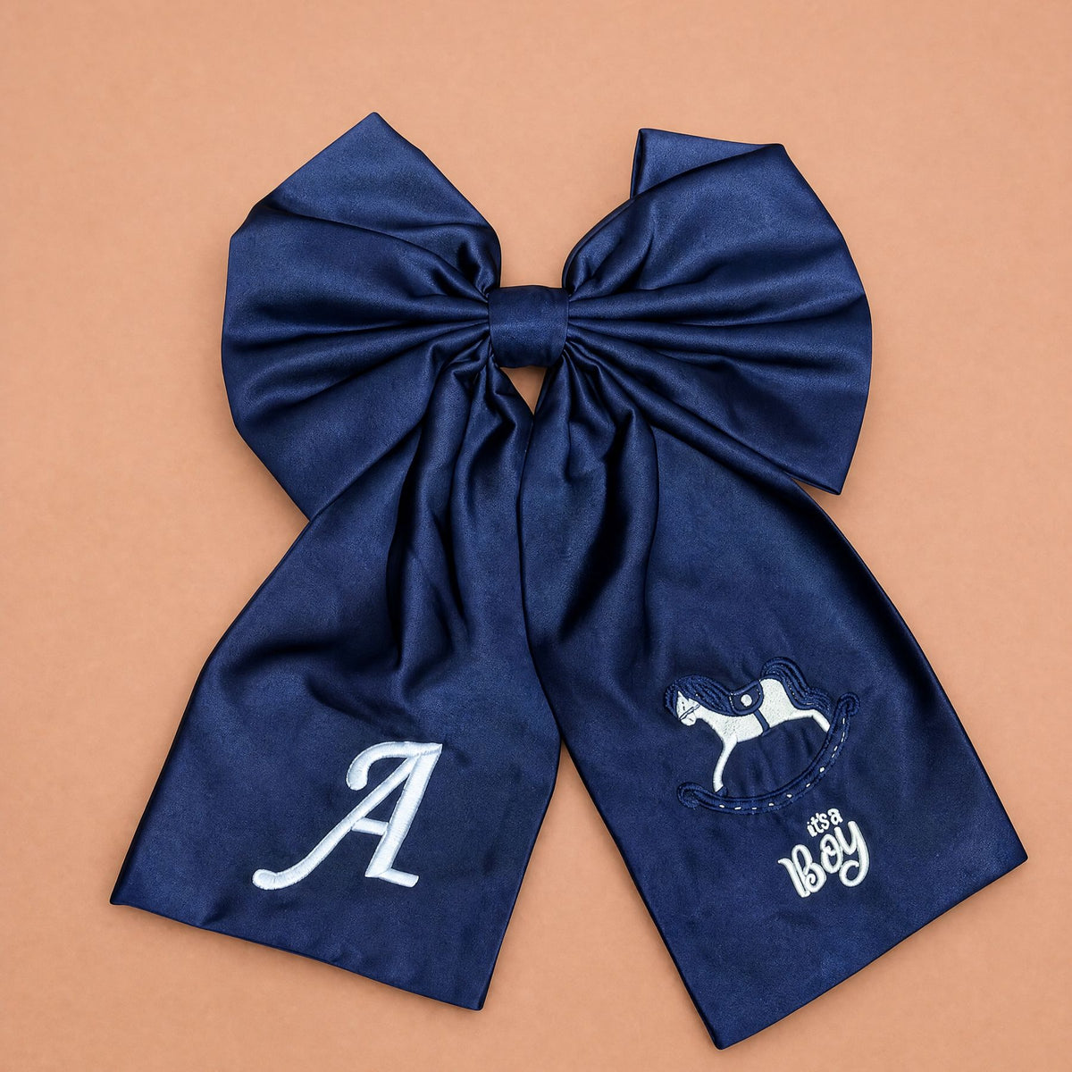 Oversized navy silk announcement bow with an embroidered ivory initial on one tail and a rocking horse with It's a Boy lettering on the other