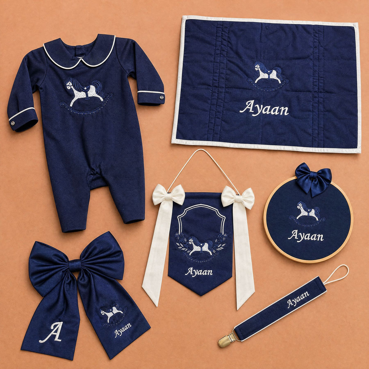 The Grand Arrival navy gift bundle laid out flat — all six personalised silk pieces including the romper, wrapping sheet, name frame, name flag, announcement bow and pacifier holder