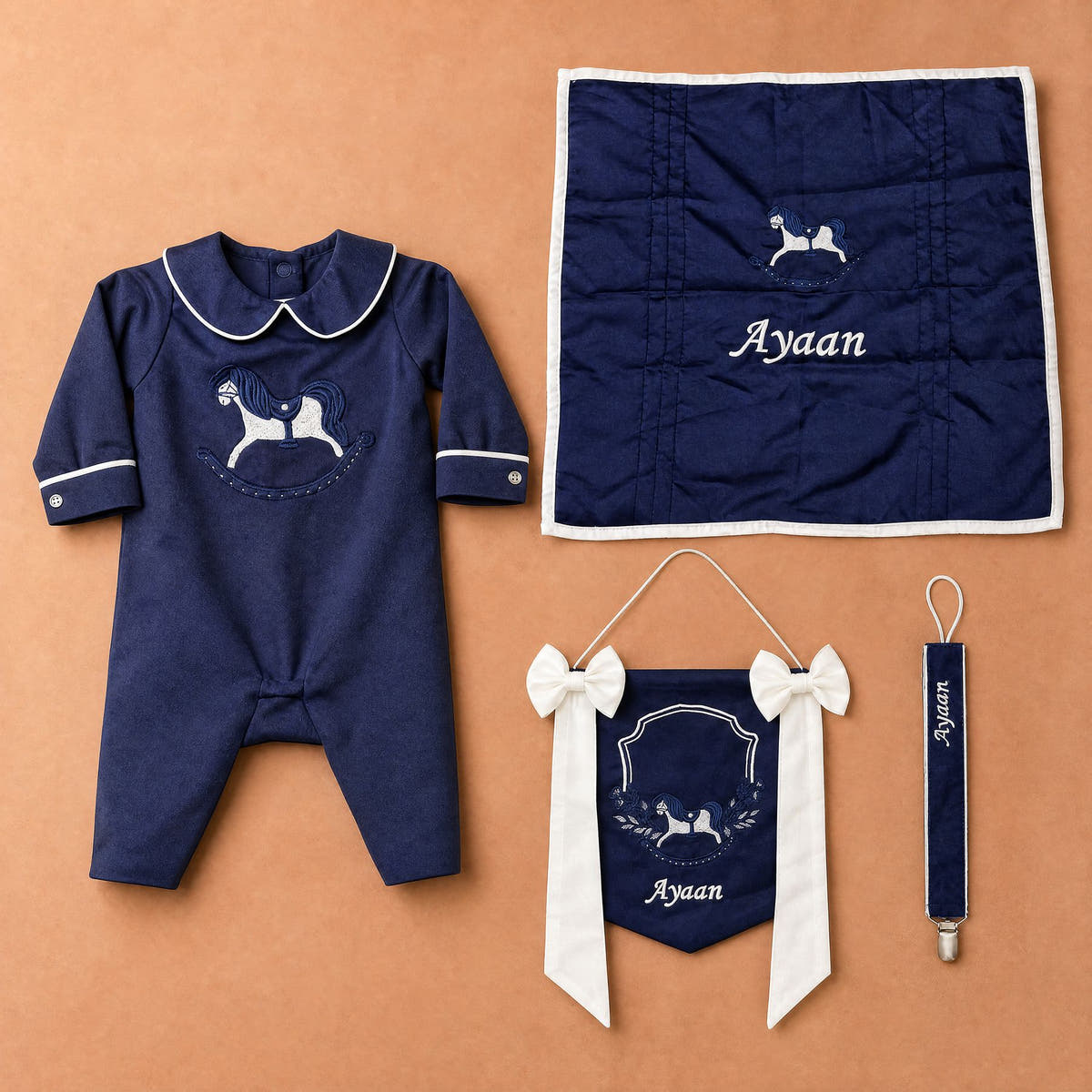 Welcome to the World navy gift bundle laid out flat — personalised silk romper, wrapping sheet, name flag and pacifier holder