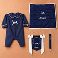 Welcome to the World navy gift bundle laid out flat — personalised silk romper, wrapping sheet, name flag and pacifier holder
