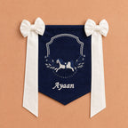 Navy silk name flag with an embroidered rocking horse crest, ivory bows and a name in ivory script