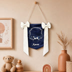 Personalised navy silk name flag hanging on a nursery wall above a teddy bear and wooden toys