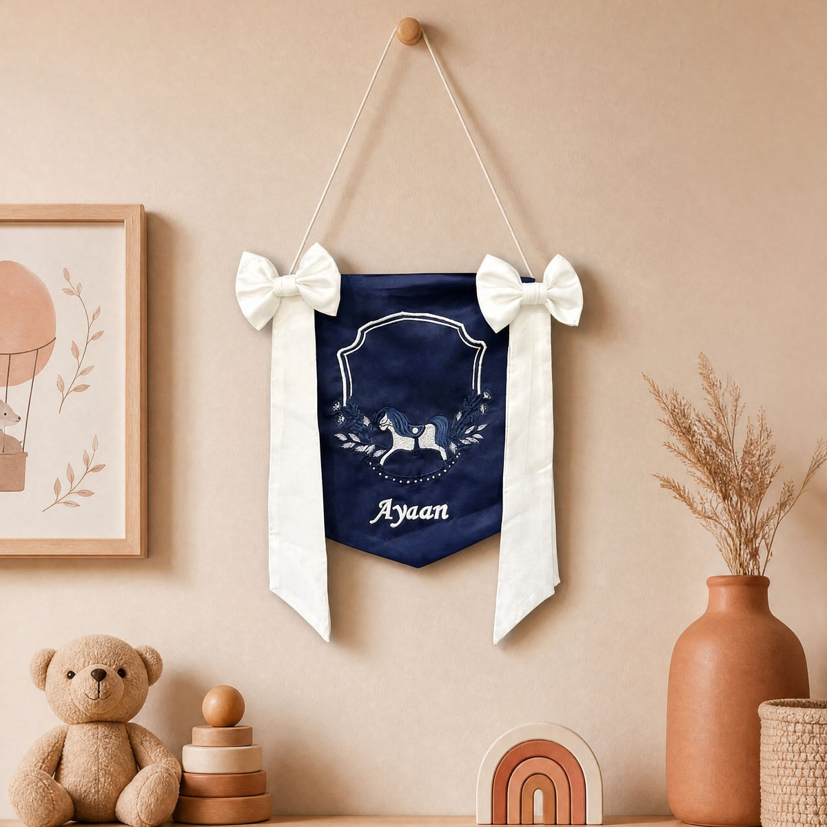 Personalised navy silk name flag hanging on a nursery wall above a teddy bear and wooden toys