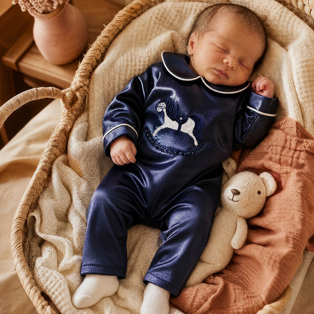 Newborn sleeping in a woven moses basket wearing the navy silk Zyra Baby romper, beside a knitted teddy