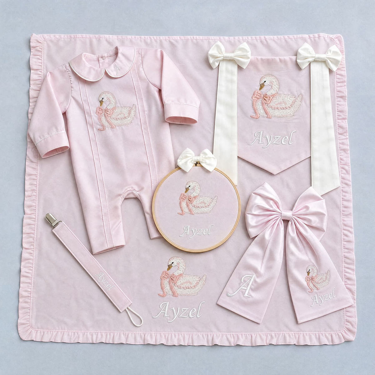 The Grand Arrival pink gift bundle laid out flat — all six personalised pink silk pieces including romper, wrapping sheet, name frame, name flag, announcement bow and pacifier holder