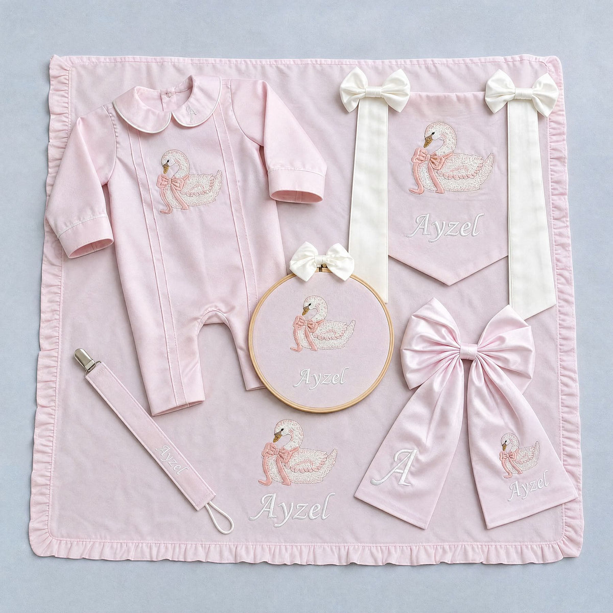 The Grand Arrival pink gift bundle laid out flat — all six personalised pink silk pieces including romper, wrapping sheet, name frame, name flag, announcement bow and pacifier holder