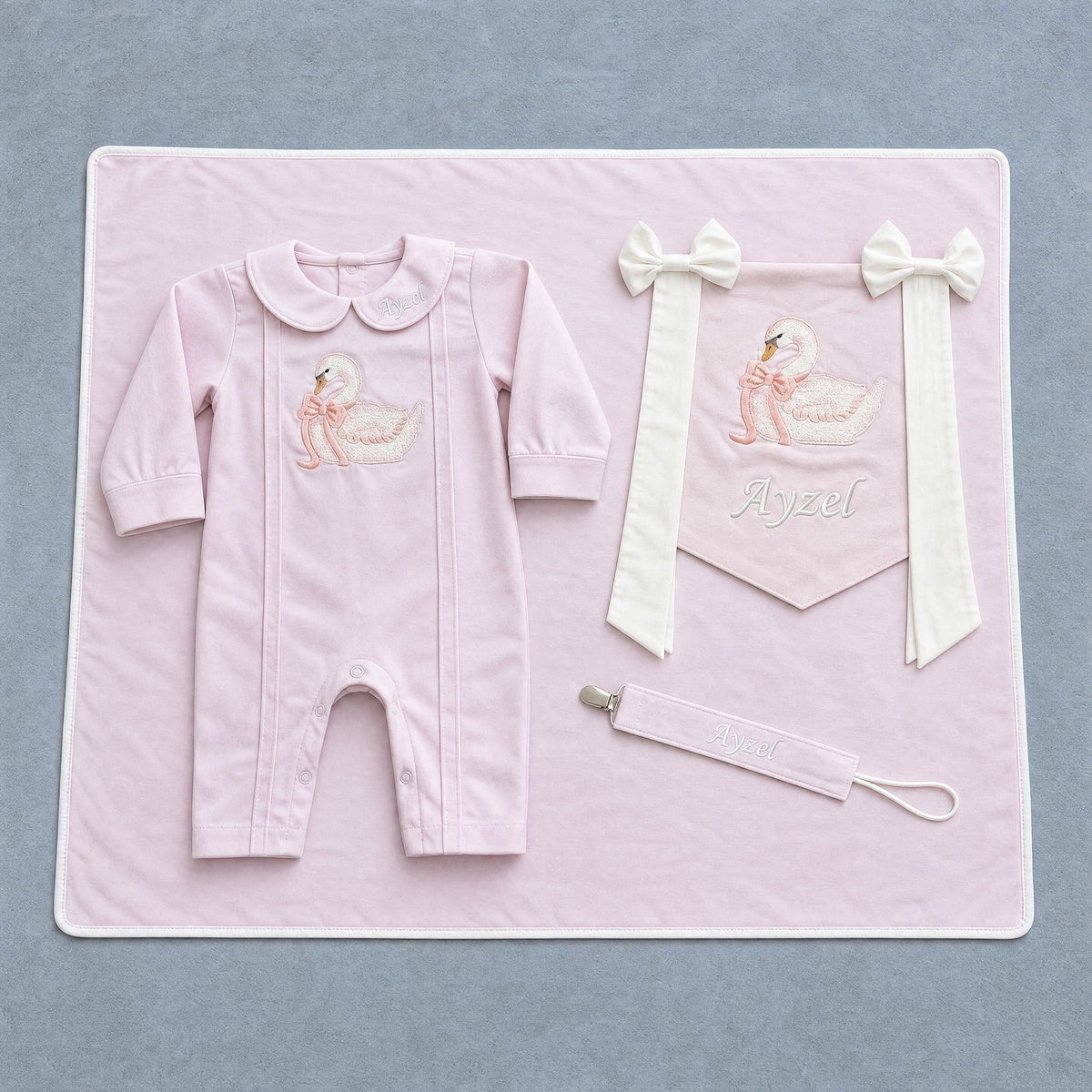 Welcome to the World pink gift bundle laid out flat — personalised pink silk romper, wrapping sheet, name flag and pacifier holder