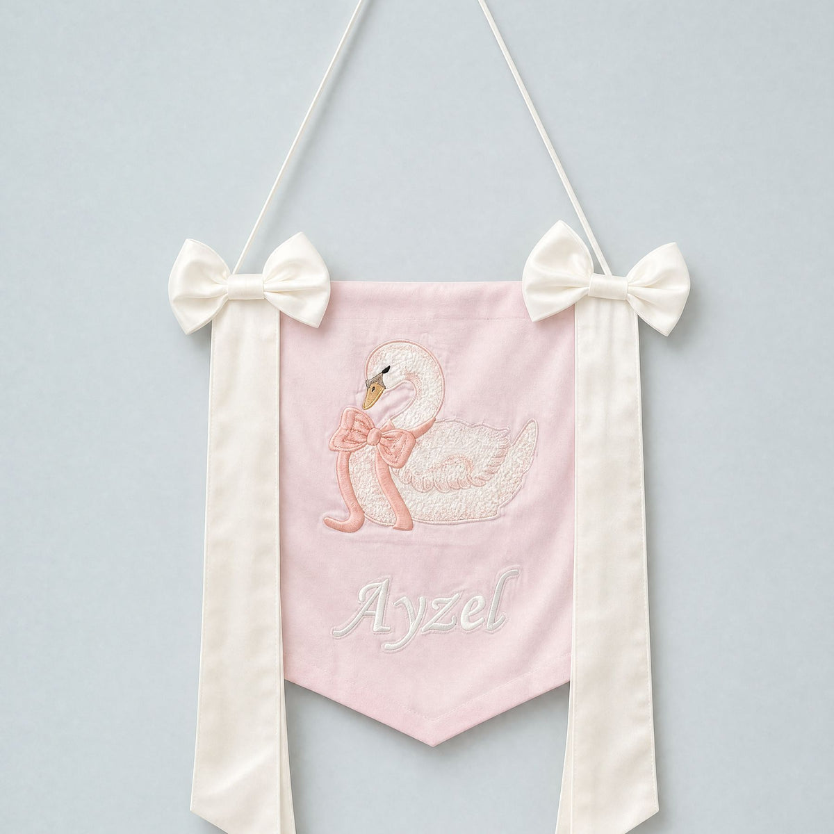Pink silk name flag with an embroidered swan, ivory silk bows and a baby's name in ivory script