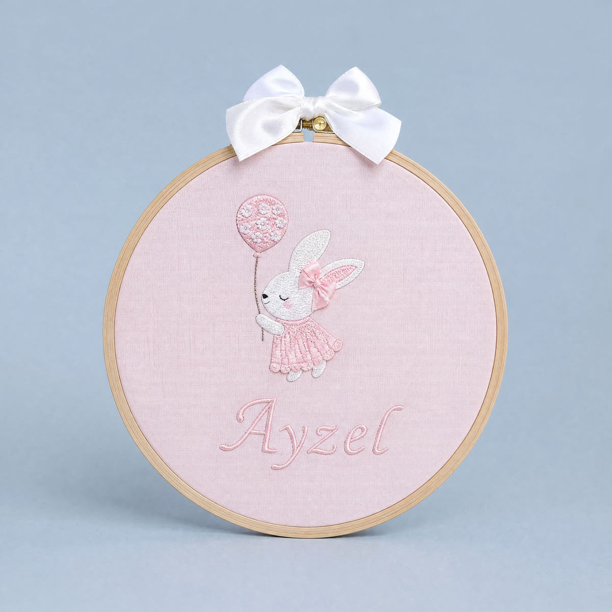 Pink embroidery hoop name frame with a bunny holding a flower-printed balloon, a white satin bow and a baby's name in pink script