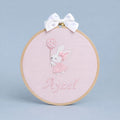 Pink embroidery hoop name frame with a bunny holding a flower-printed balloon, a white satin bow and a baby's name in pink script