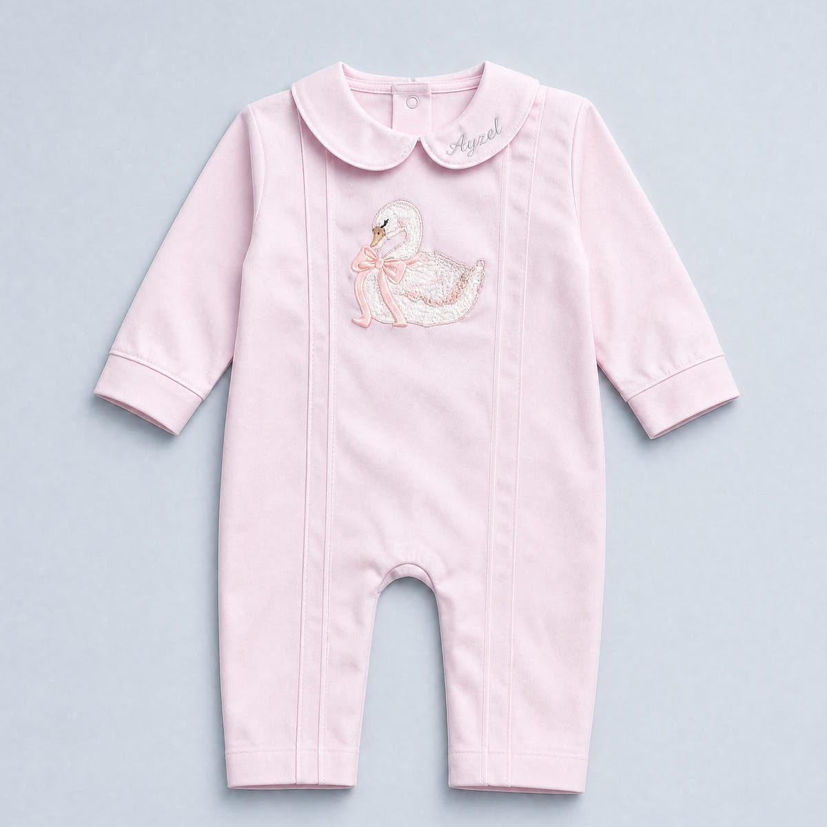 Soft pink silk baby romper with a Peter Pan collar, tonal piping and an embroidered white swan with a pink ribbon bow at the chest
