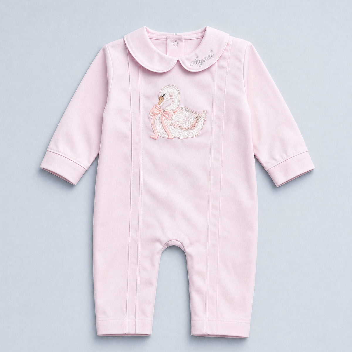 Soft pink silk baby romper with a Peter Pan collar, tonal piping and an embroidered white swan with a pink ribbon bow at the chest