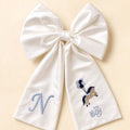 Oversized ivory silk announcement bow with a pale blue embroidered initial on one tail and a pony holding balloons with It's a Boy lettering on the other
