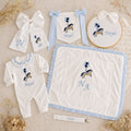 The Grand Arrival white and blue gift bundle laid out flat — all six personalised ivory silk pieces including romper, wrapping sheet, name frame, name flag, announcement bow and pacifier holder
