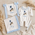 Welcome to the World white and blue gift bundle laid out flat — personalised ivory silk romper, wrapping sheet, name flag and pacifier holder