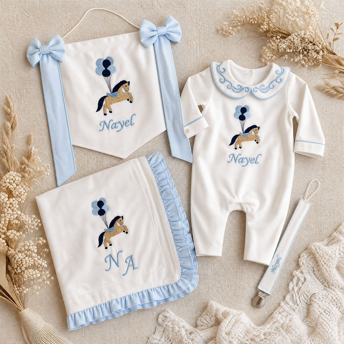 Welcome to the World white and blue gift bundle laid out flat — personalised ivory silk romper, wrapping sheet, name flag and pacifier holder