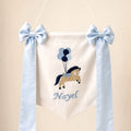 Ivory silk name flag with an embroidered pony and balloons, silk bows and a baby's name in pale blue script