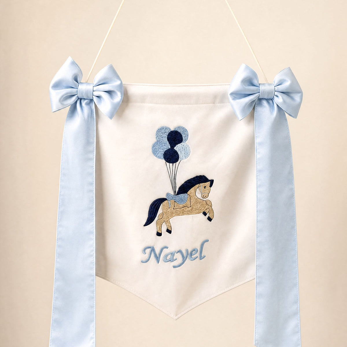 Ivory silk name flag with an embroidered pony and balloons, silk bows and a baby's name in pale blue script