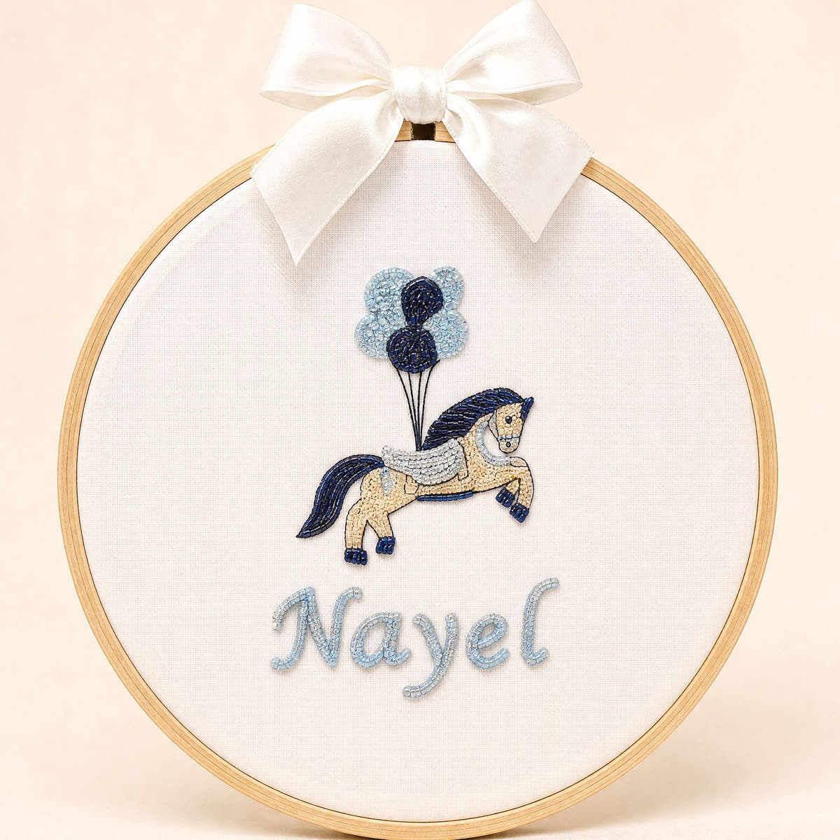 Ivory silk name frame in a light wooden hoop with an embroidered pony and balloons and a name in pale blue script