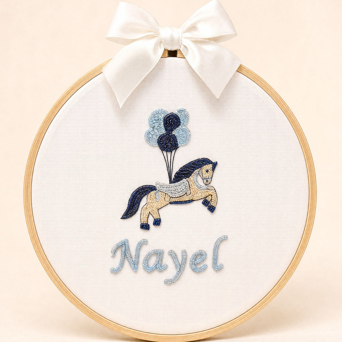 Ivory silk name frame in a light wooden hoop with an embroidered pony and balloons and a name in pale blue script