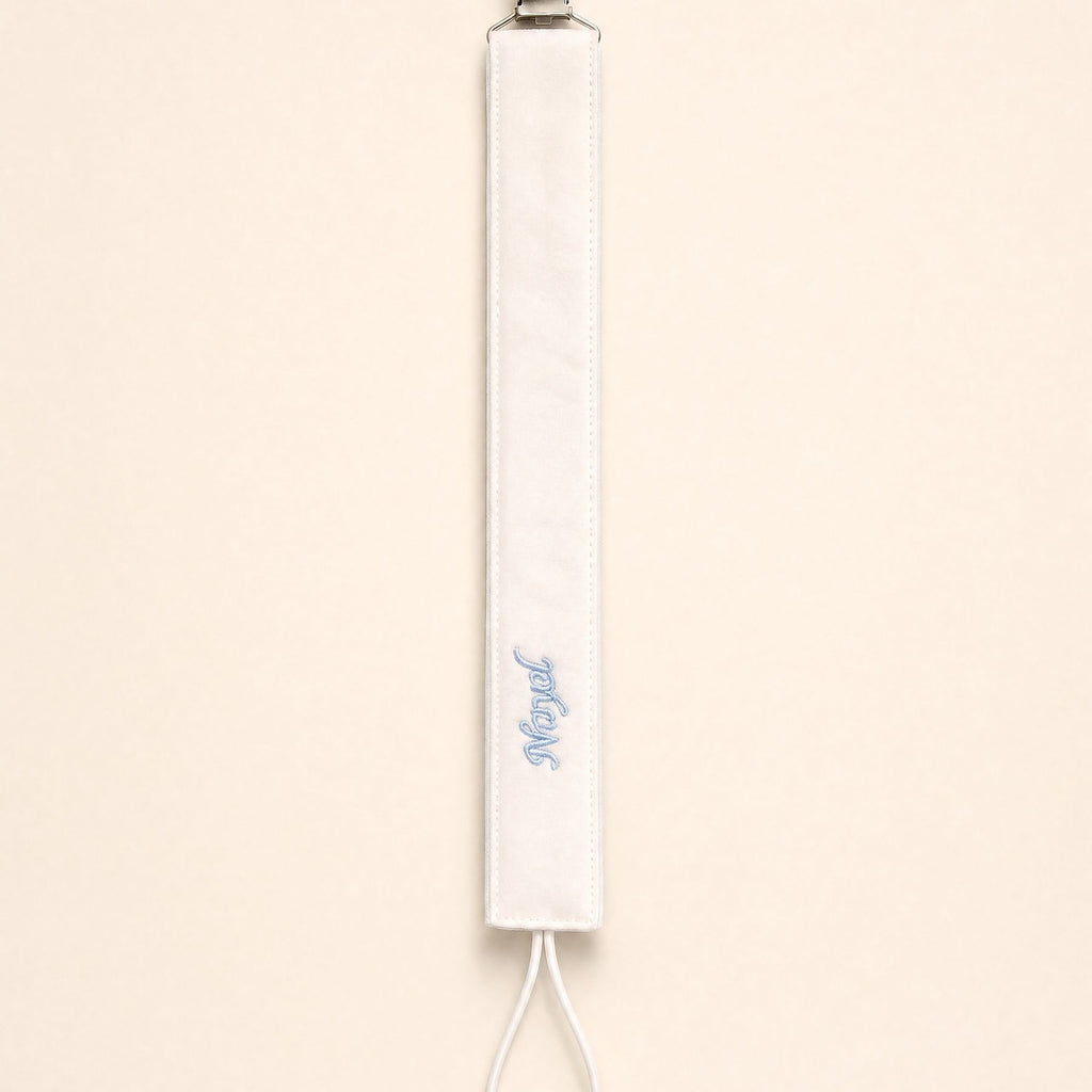 Ivory silk pacifier holder with pale blue detailing and a baby's name embroidered in pale blue script