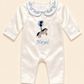 Ivory silk baby romper with pale blue piping, a scrolled Peter Pan collar and an embroidered tan pony holding pale blue and navy balloons