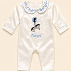 Ivory silk baby romper with pale blue piping, a scrolled Peter Pan collar and an embroidered tan pony holding pale blue and navy balloons