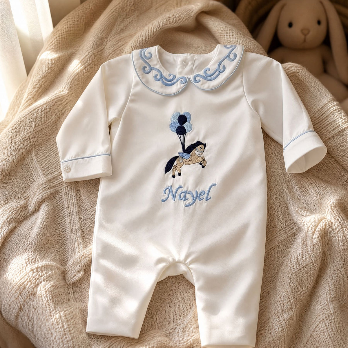 Ivory silk Zyra Baby romper with pale blue detailing, styled in a nursery setting