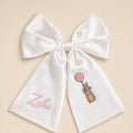 Large ivory silk announcement bow with a baby's name in pink on one tail and an embroidered bunny holding a pink balloon on the other