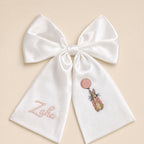 Large ivory silk announcement bow with a baby's name in pink on one tail and an embroidered bunny holding a pink balloon on the other