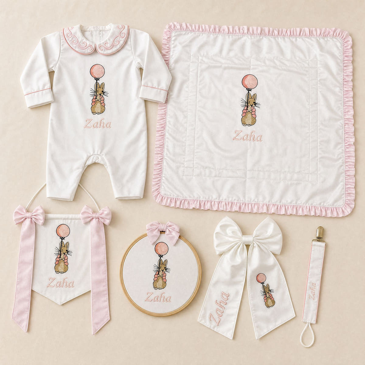 The Grand Arrival white and pink gift bundle laid out flat — all six personalised ivory silk pieces including romper, wrapping sheet, name frame, name flag, announcement bow and pacifier holder