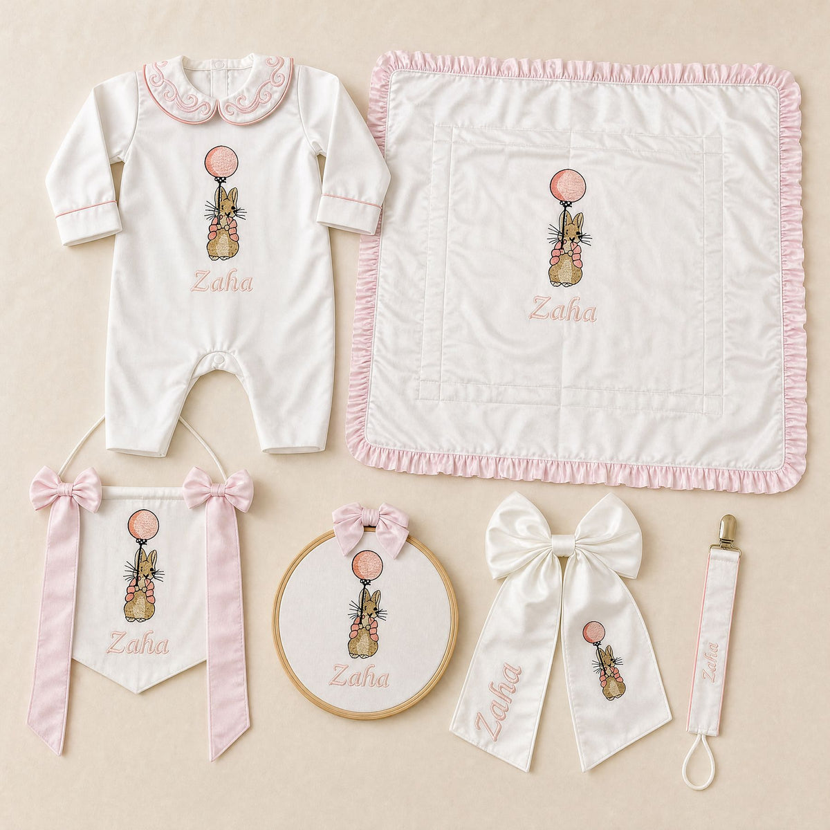 The Grand Arrival white and pink gift bundle laid out flat — all six personalised ivory silk pieces including romper, wrapping sheet, name frame, name flag, announcement bow and pacifier holder
