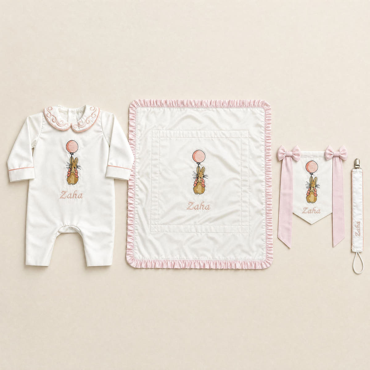 Welcome to the World white and pink gift bundle laid out flat — personalised ivory silk romper, wrapping sheet, name flag and pacifier holder