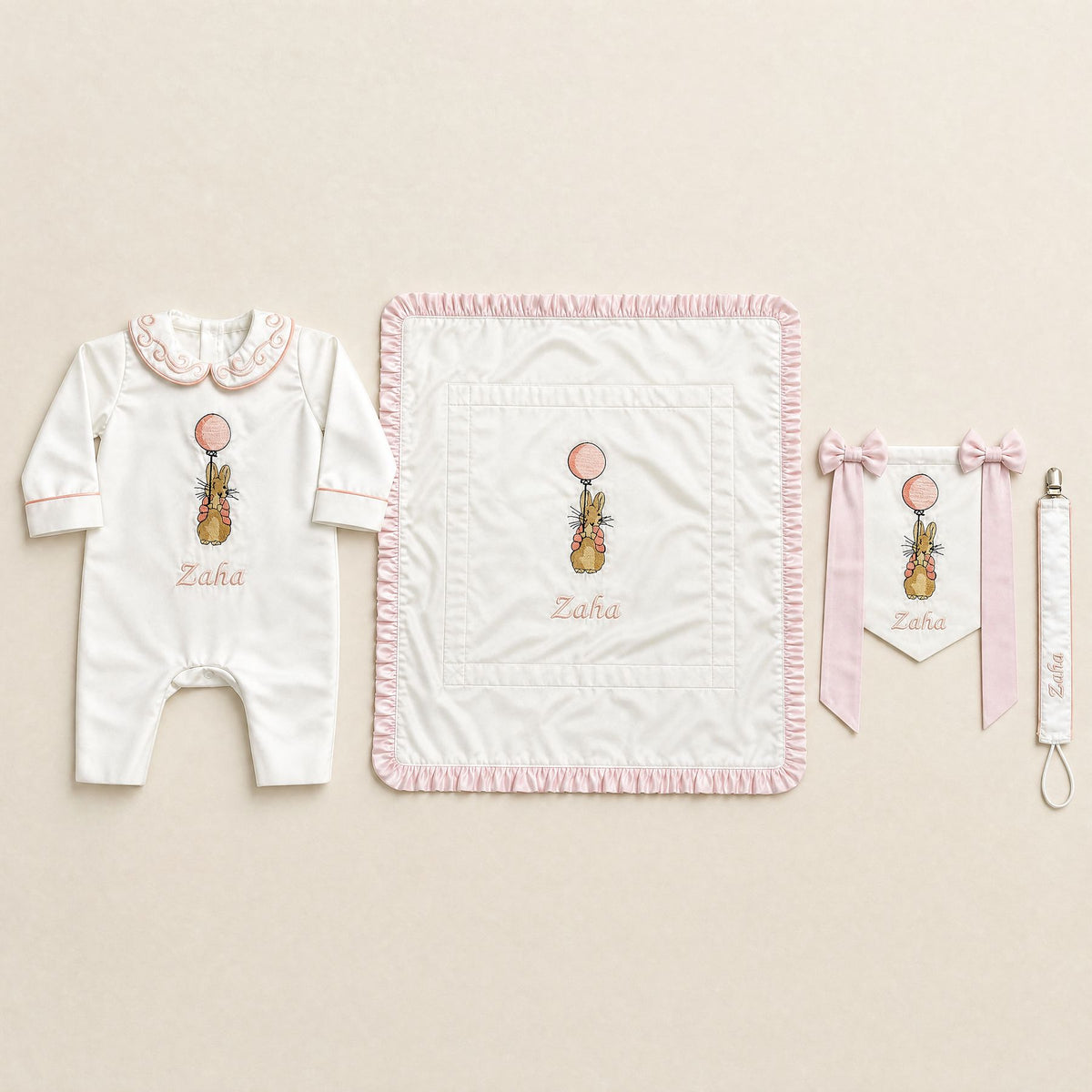 Welcome to the World white and pink gift bundle laid out flat — personalised ivory silk romper, wrapping sheet, name flag and pacifier holder