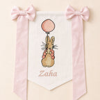 Ivory silk name flag with an embroidered bunny holding a pink balloon, soft pink silk bows and a baby's name in pink script